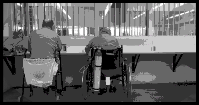 two elderly inmates in wheelchairs looking through bars